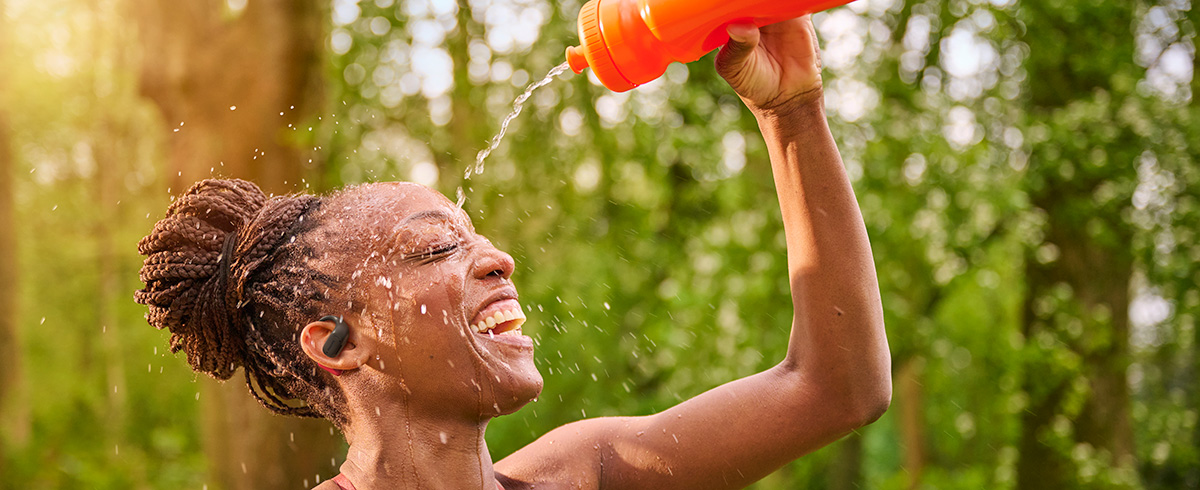 Vrouw verfrist zich door water over haar hoofd te gieten terwijl ze buiten een Philips sporthoofdtelefoon draagt